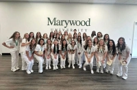 A group of nursing students in their white uniforms, standing in front of a white wall with a green Marywood wordmark on it. Nursing Graduates Achieve 100% Pass Rate on National Licensure Exam for Third Consecutive Year