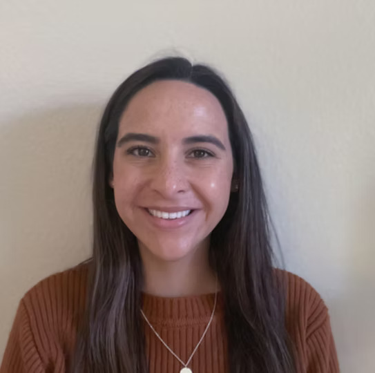girl smiling in front of white wall with dark orange sweater and black hair
