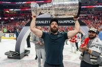 Man with a beard holding the silver Stanley Cup in an ice rink.