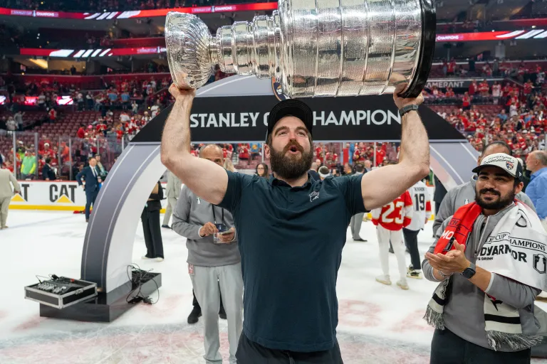 Man with a beard holding the silver Stanley Cup in an ice rink.
