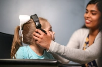 A female student places a set of headphones over the ears of a young child