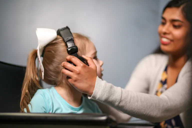 A female student places a set of headphones over the ears of a young child