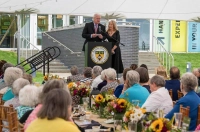 People at a podium in front of a crowd sitting at tables with flowers