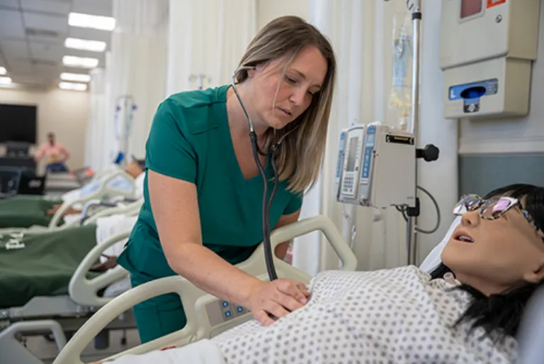 nursing student checking heartbeat on dummy using stethoscope