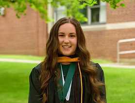 girl standing in grass field wearing graduation gown and medals around her neck