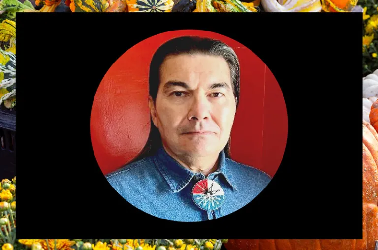 Man with dark hair in a denim shirt against a red background on top of a black square