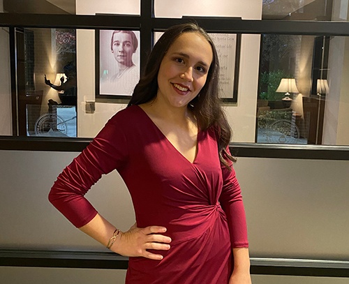 Young woman smiling wearing a red dress in front of a window