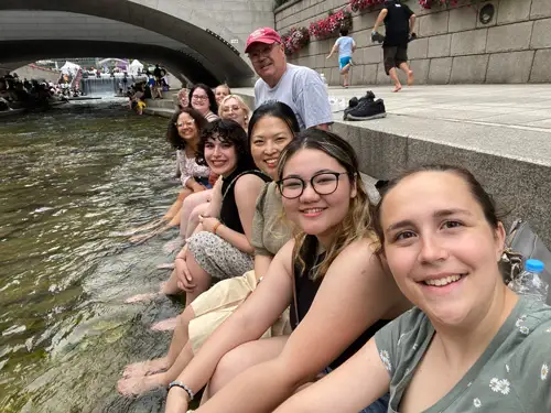 a group of music therapy student, including Sophie French, sitting a long side a river and smiling.