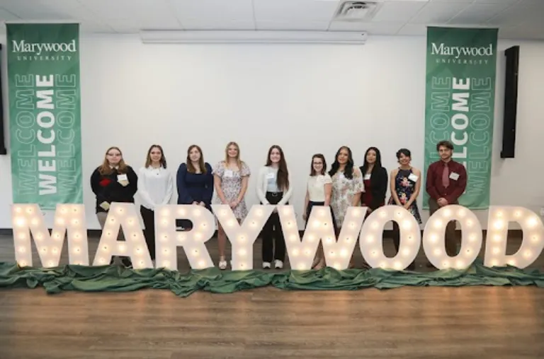 Students gather around lighted letters that spell out MARYWOOD.