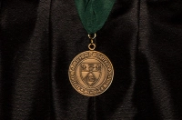 A gold engraved Marywood commencement medal on a green ribbon against a black graduation robe