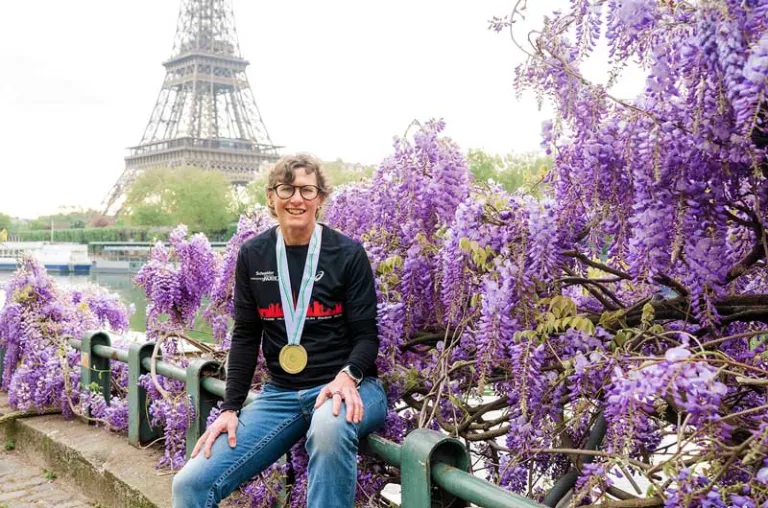 Woman in Paris, wearing a marathon medal in front of purple flowers with the Eiffel Tower in the background.